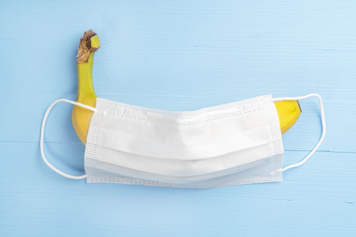 yellow banana under a white medical protective mask on a wooden light blue background
