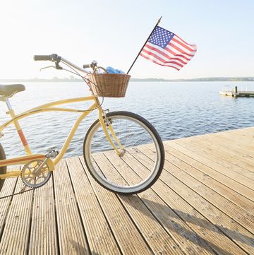 yellow beachcruiser bicycle with united states flag blowing in the wind on a jetty at an idyllic lake in summer against blue sky