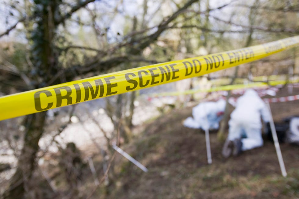 Yellow crime scene tape in front of a murder scene being investigated by police.
