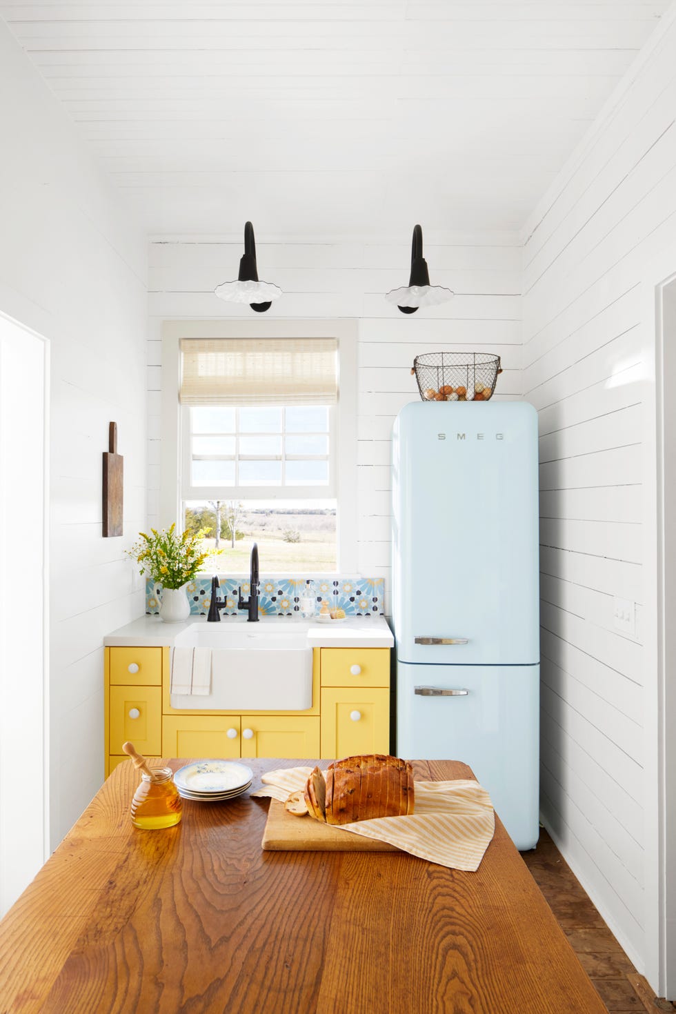 Small farmhouse kitchen with bright yellow cabinets and a light blue Smeg refrigerator