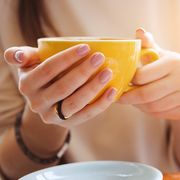 Yellow mug in the hands of a young woman. Girl holding a Cup of coffee in a cafe. Coffee break, Breakfast. The concept of power. Close up.