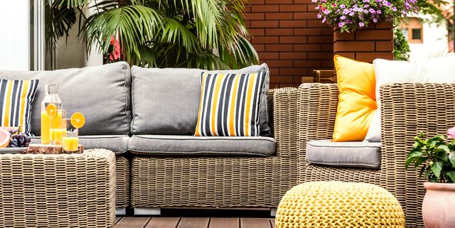 Yellow pouf next to rattan armchair on wooden terrace with striped pillows on sofa