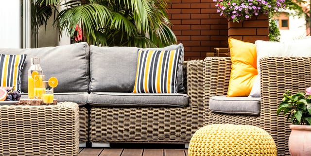 Yellow pouf next to rattan armchair on wooden terrace with striped pillows on sofa