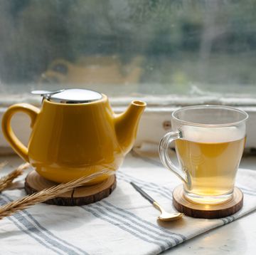 yellow teapot and glass cup with herbal tea on the window sill