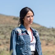 kelsey asbille in a field talking to rainwater she is wearing a long floral print skirt and jean jacket with western embroidery and  strand of long red beads