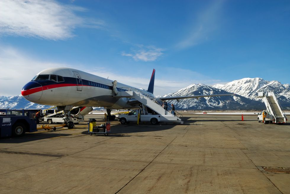 people boarding a jet airplane with snow covered mountains in background