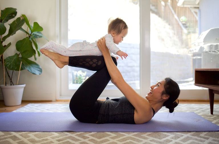 Side View Of Happy Woman Playing With Baby While Exercising At Home
