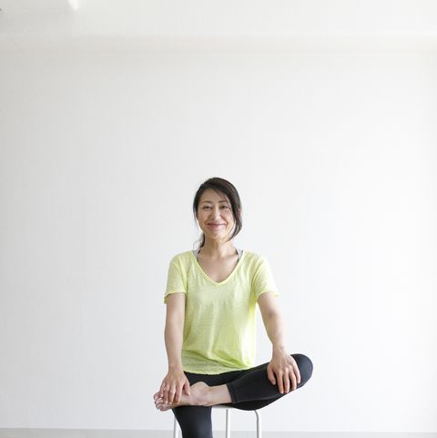 young woman sitting in a chair demonstrating a supported figure four yoga pose