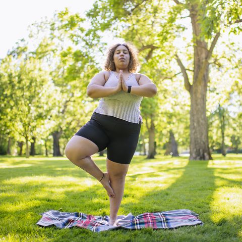 young woman demonstrating yoga tree pose outdoors in a park