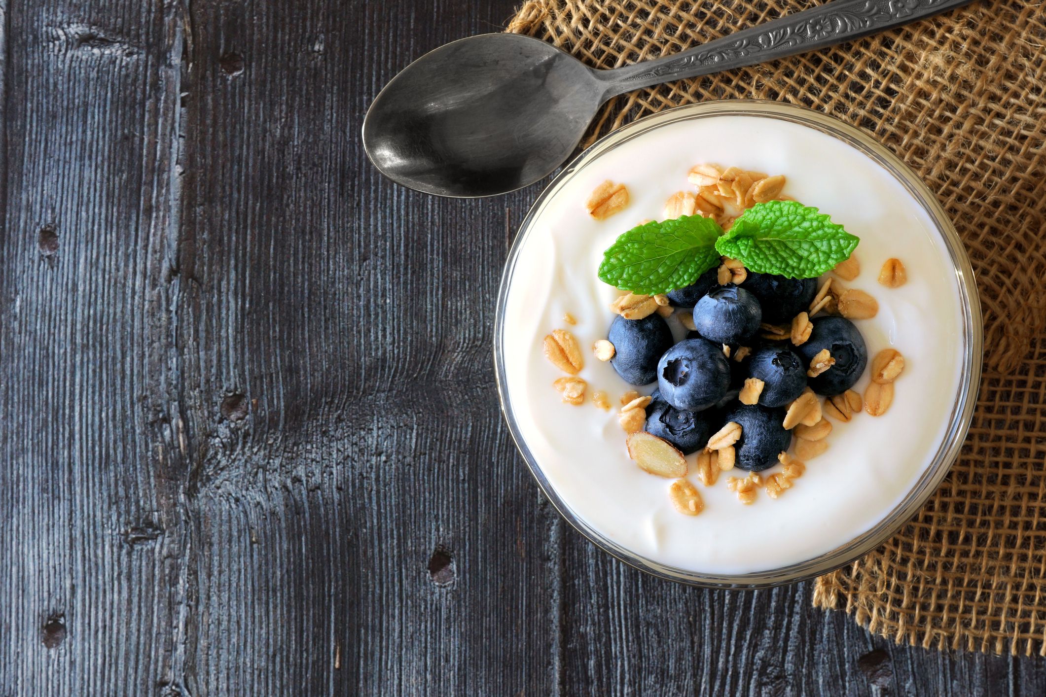 Yogurt with blueberries, granola, above view on rustic dark wood