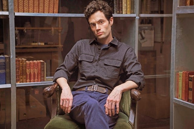 penn badgley posa sentado, mirando a cámara, en una foto promocional de la serie you