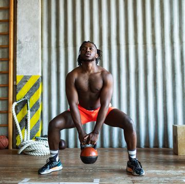 young adult black man doing kettlebell squats in gym