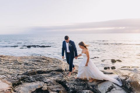 young adult couple in wedding dress and suit walking on the cliffs on the coast of porto, portugal