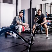 Young Adult Man Swinging Ropes While Fitness Instructor Motivates Him