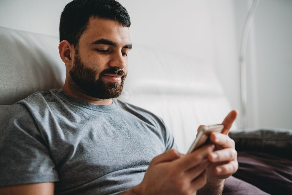 young adult man using his smartphone sitting on the sofa