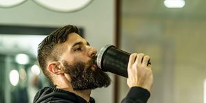 young adult man with beard drinking bottle supplement shake in training at gym side view copy space real people