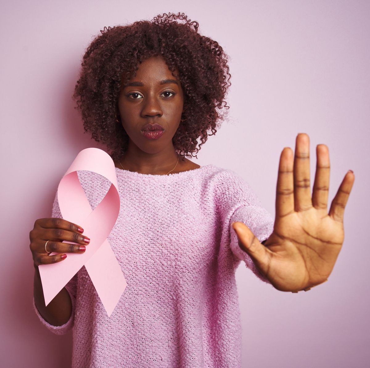 young african afro woman holding cancer ribbon standing over isolated pink background with open hand doing stop sign with serious and confident expression, defense gesture