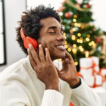 young african american man using headphones sitting by christmas tree at home