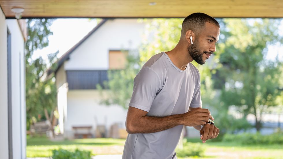 young african american sportive man listening to music in wireless earphones looking at smart watch