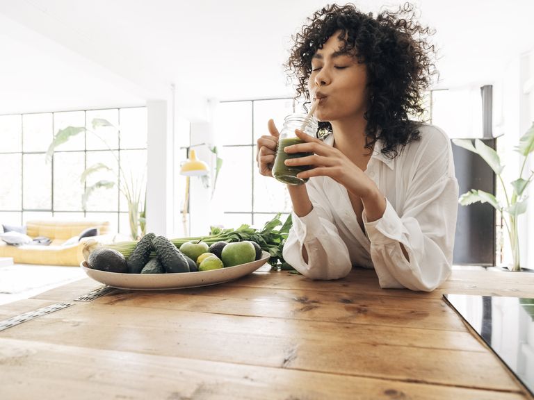 young african american woman drinking green juice with reusable bamboo straw in loft apartment copy space