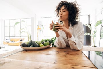 young woman drinking green juice with reusable bamboo straw in loft apartment copy space