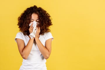 a woman blows her nose on a yellow background