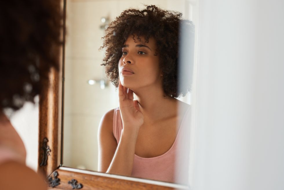 woman examining her skin in a bathroom mirror