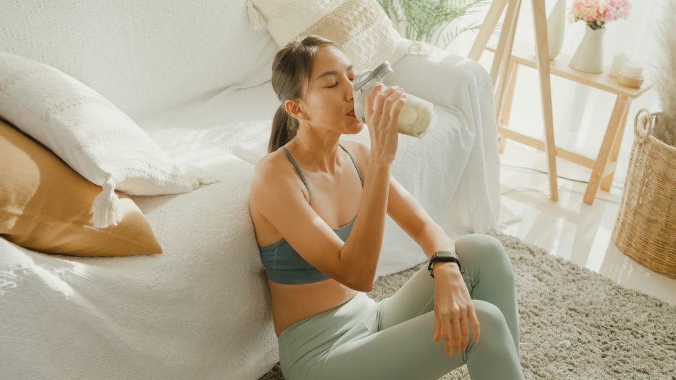 young asian athletic woman drinking protein shake in living room at home diet and healthy food