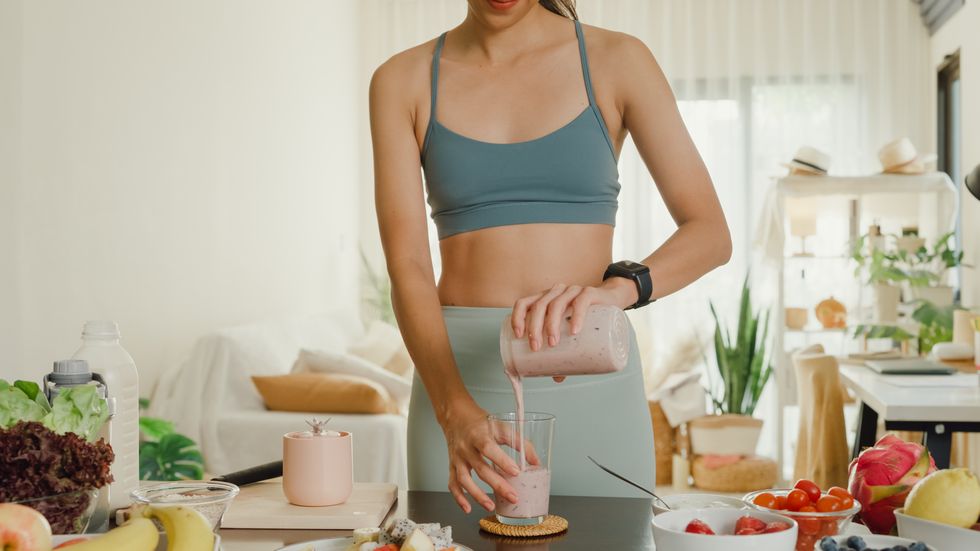 young asian athletic woman using blender and pouring smoothie to glass at home healthy food