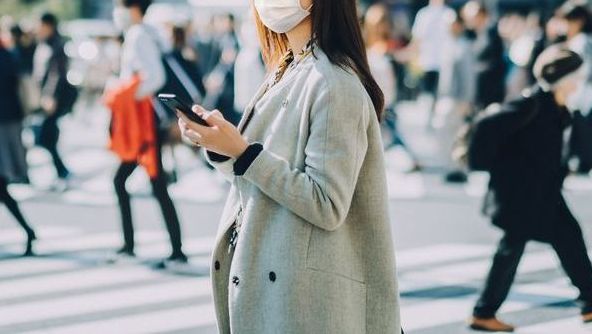 young asian businesswoman commuting in busy downtown city street with protective face mask and using smartphone to protect and prevent from the spread of viruses during covid 19 health crisis