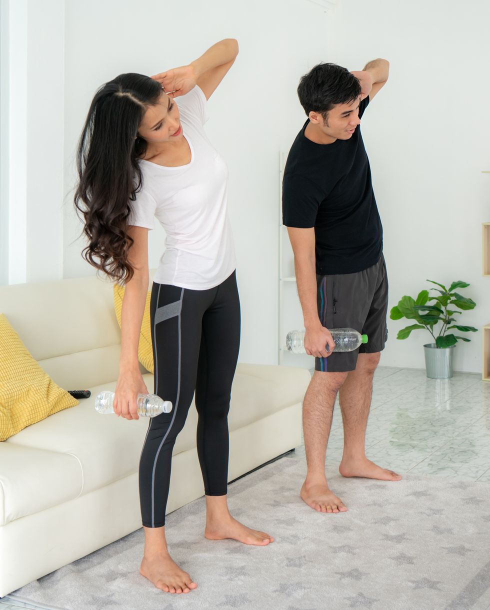 young asian couple doing high intensity interval training together and looking tv at home, man and woman working out together standing in living room, fit pair performing fitness exercise with partner