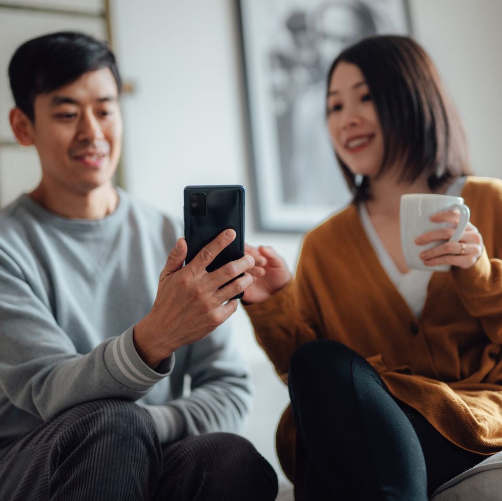 young asian couple shopping online with smart phone, sitting on sofa at home