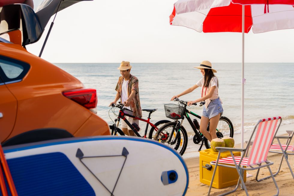 young asian couple with bicycles walking along sea beach on summer day
