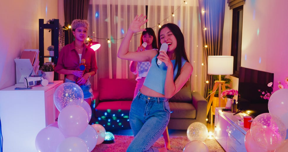 young asian female friends singing karaoke having fun at colorful house party at night