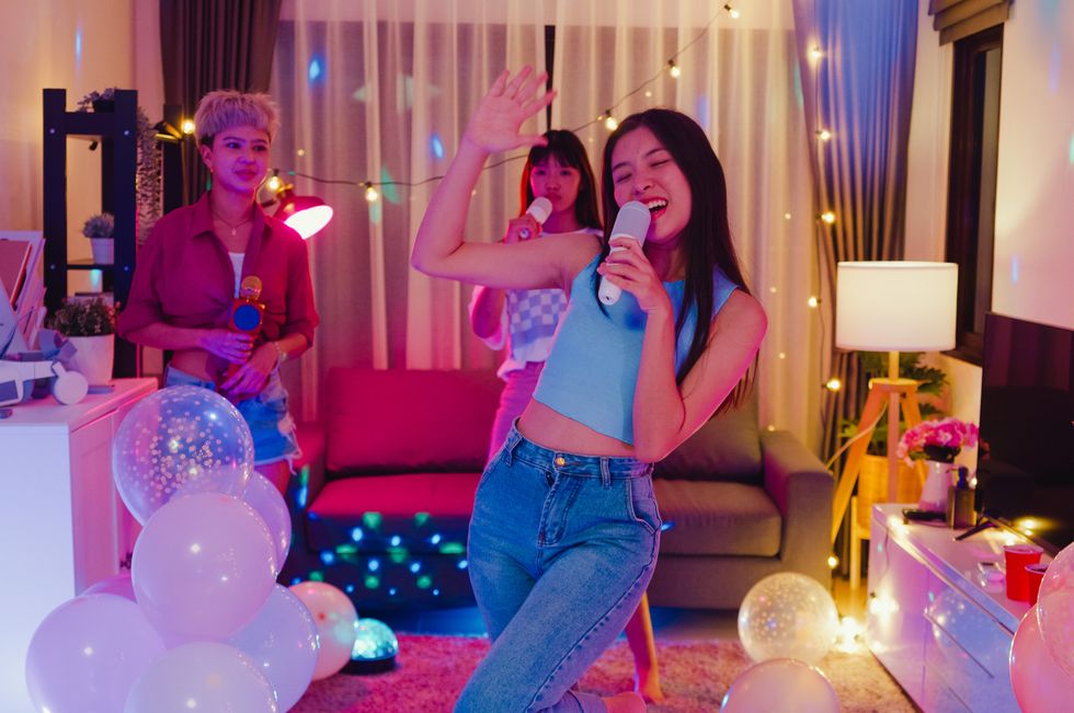 young asian female friends singing karaoke having fun at colorful house party at night