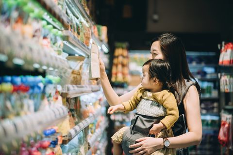young asian mother grocery shopping with little daughter and choosing for organic baby food in the supermarket