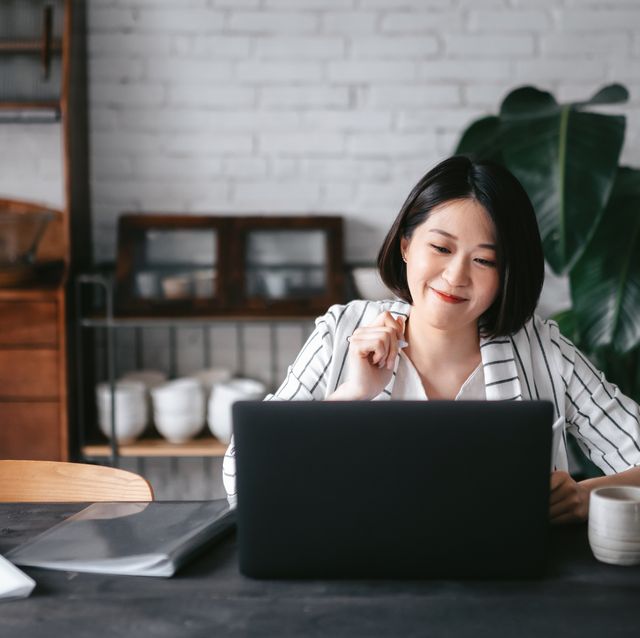 young asian woman having online business meeting, video conferencing on laptop with her business partners, working from home in the living room