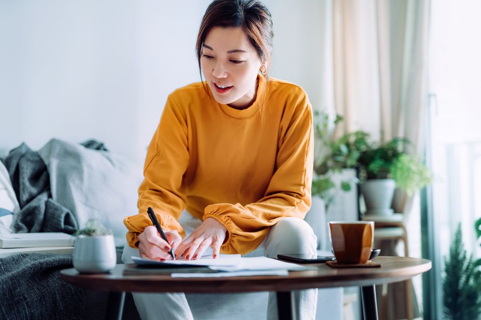 young asian woman holding a pen and signing paperwork in the living room at home deal concept
