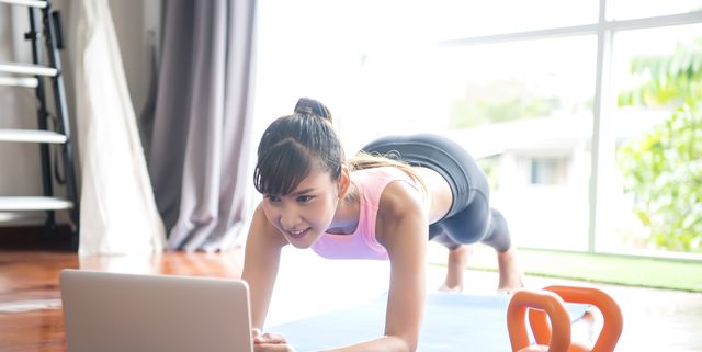 young asian woman in sportswear watching online video with fitness exercises on laptop and doing planks position at home distant training with personal trainer in living room at home practicing  workout at home healthy lifestyle, social distancing conc