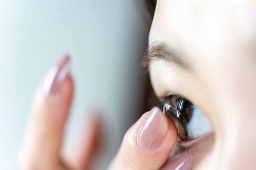 young woman inserting a brown contact lens in eye