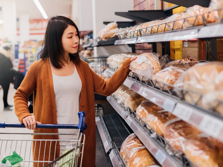 Young Asian woman picking up bread in grocery store with a trolley