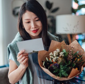 young woman reading greeting card attached and holding flower bouquet