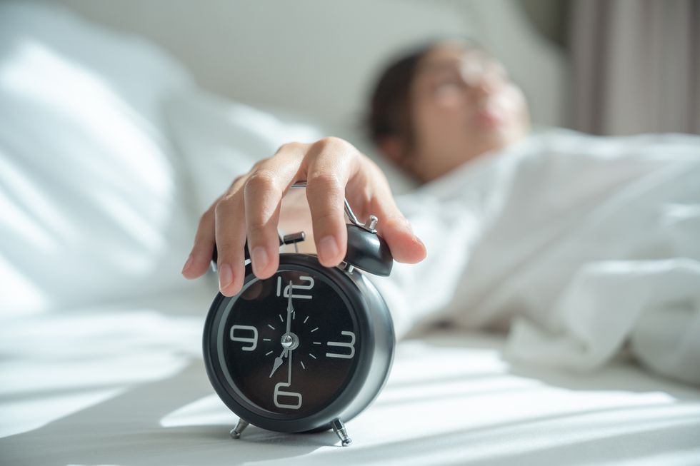 young asian woman wake up early in morning female lying on bed and trying turn off alarm clock young sleeping woman and alarm clock in bedroom at home