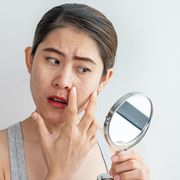 young asian woman worry about her face when she saw the problem of acne and scar by the mini mirror