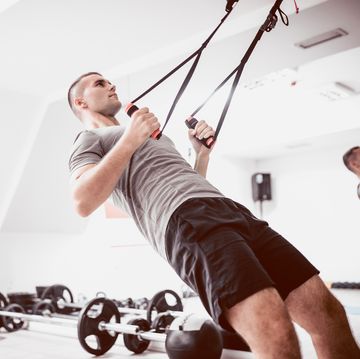 young athlete men doing back exercise with suspension straps in gym