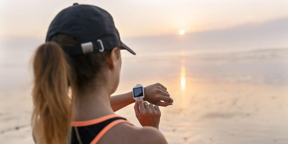 young athlete woman looking the smartwatch on the beach at sunset