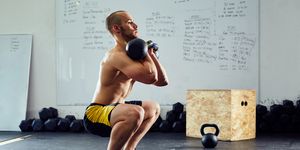 Young athletic man doing squats with kettlebells at the gym