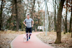 young athletic man jogging with dog on sports track