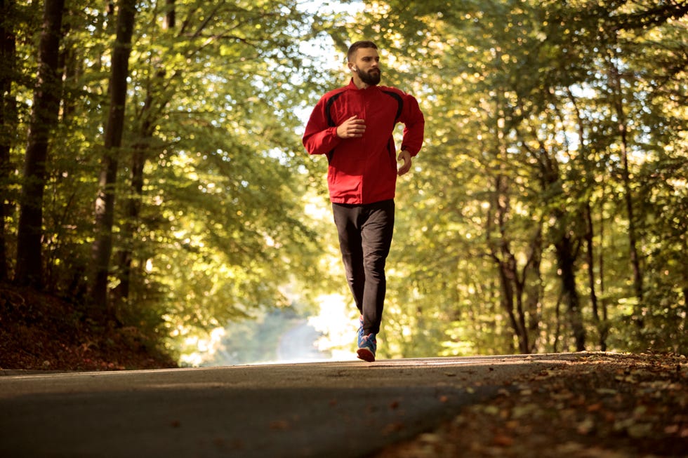 young athletic man with bluetooth headphones jogging in forest