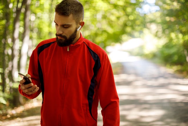 young athletic man with bluetooth headphones using mobile phone while jogging in forest